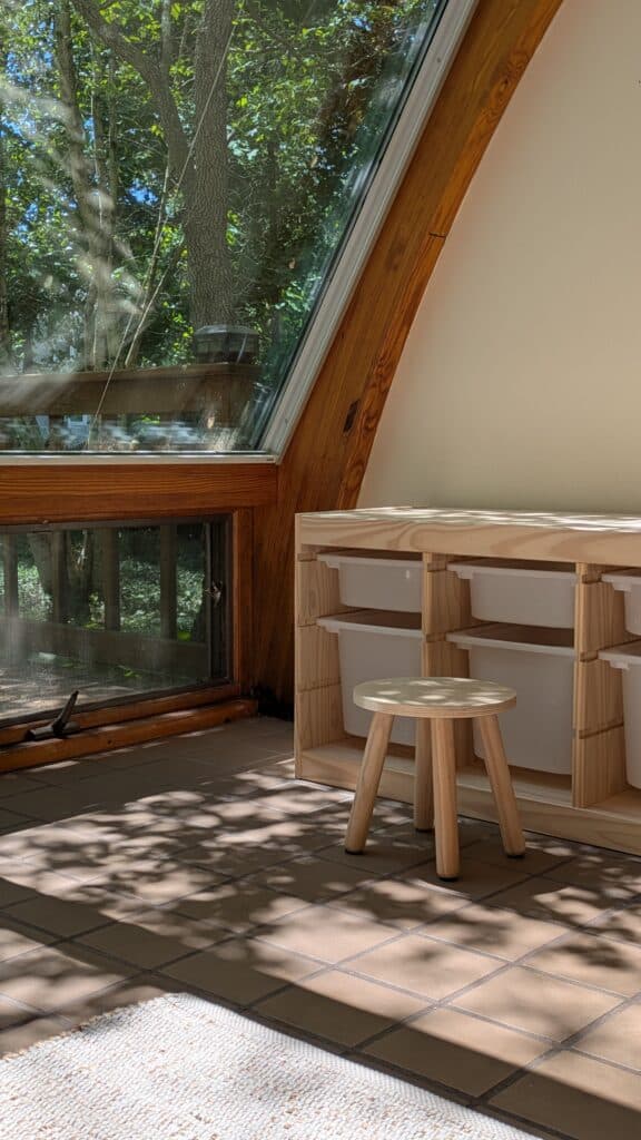 Sunroom with nautral light coming in, the leaves dancing on the ground. Toy storage unit with a small kids stool. 