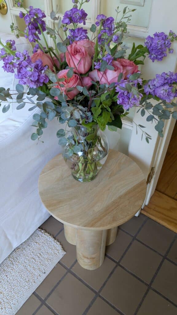 An accent table with a glass vase and beautiful flower arrangement. 