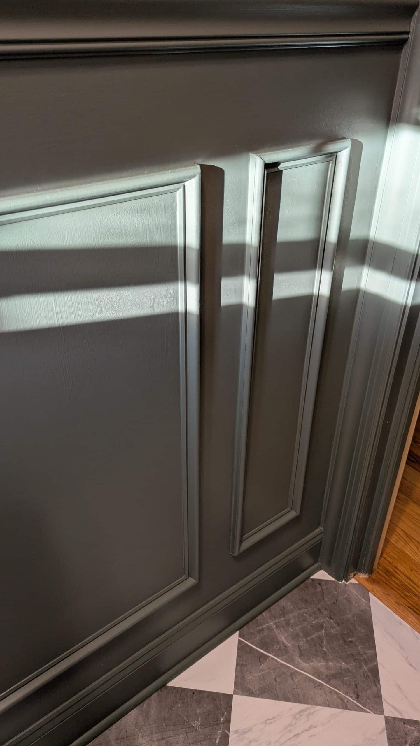 An image of dark green moody paint with DIY wainscotting. Also marble checkered tiles.