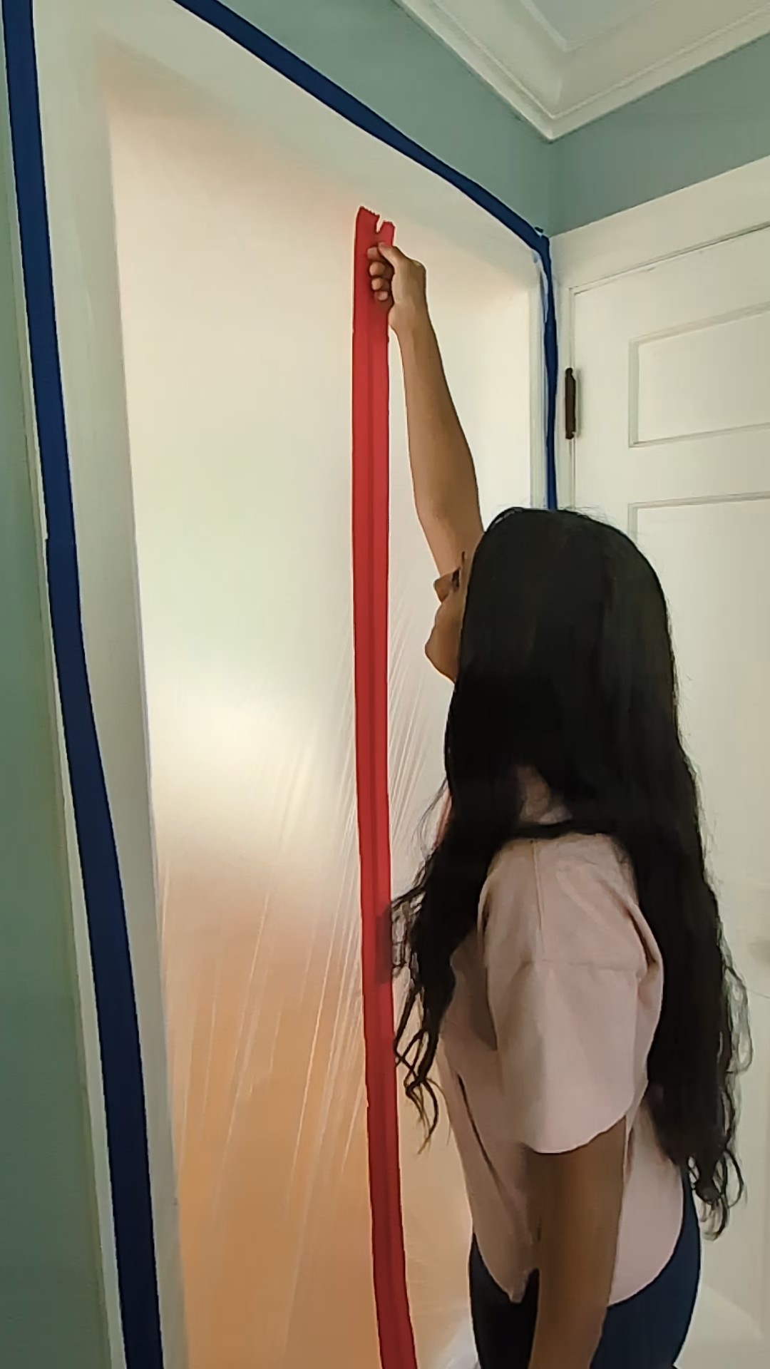 A plastic sheet on a door with a red zipper going down the middle. A woman opening the door zipper. DIY door dust barrier.