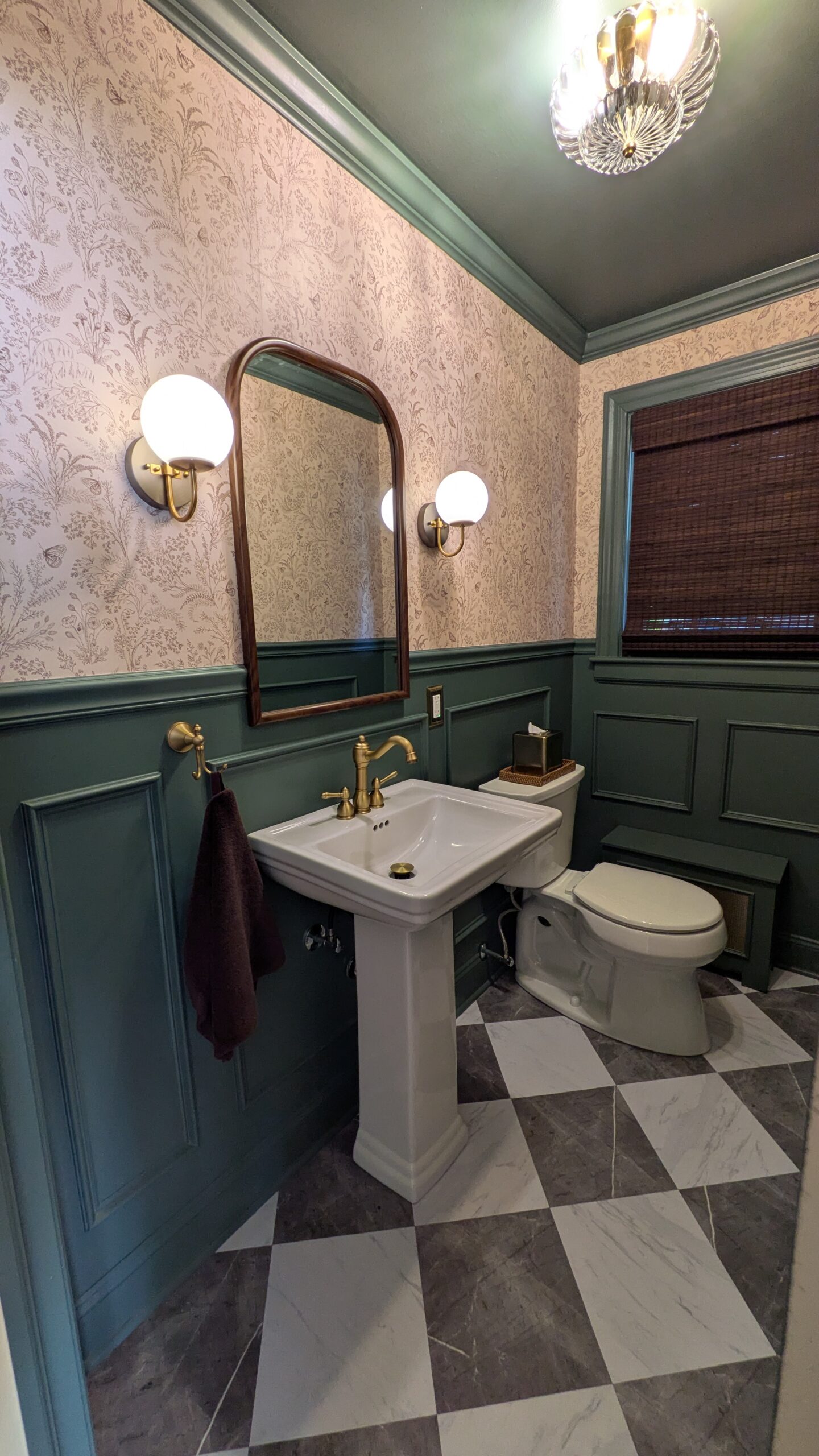 Half Bathroom Makeover mood and green with beautiful beige wallpaer and nice globe sconces along with pedestal sink and toilet and a gorgeous bamboo window treatment.