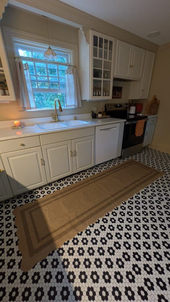 No demo kitchen renovation on a budget in this image includes new brass faucet, danty ceramic pendant light, unique red tomato vase, serving boards against the wall, wall art above the kitchen a candle burning with cafe curtains hung up on the window.
