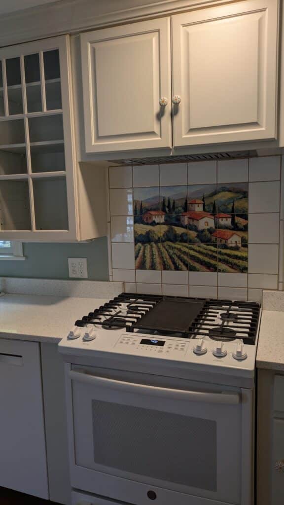 White kitchen cabinets with white stove and a vineyard villas tile mural above the stove.