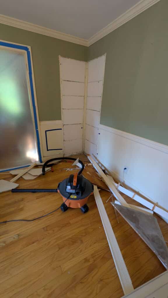 Dining room DIY makeover. An image of a shop vaccum on the floor. Baseboard trims removed and a corner built-in hutch removed.