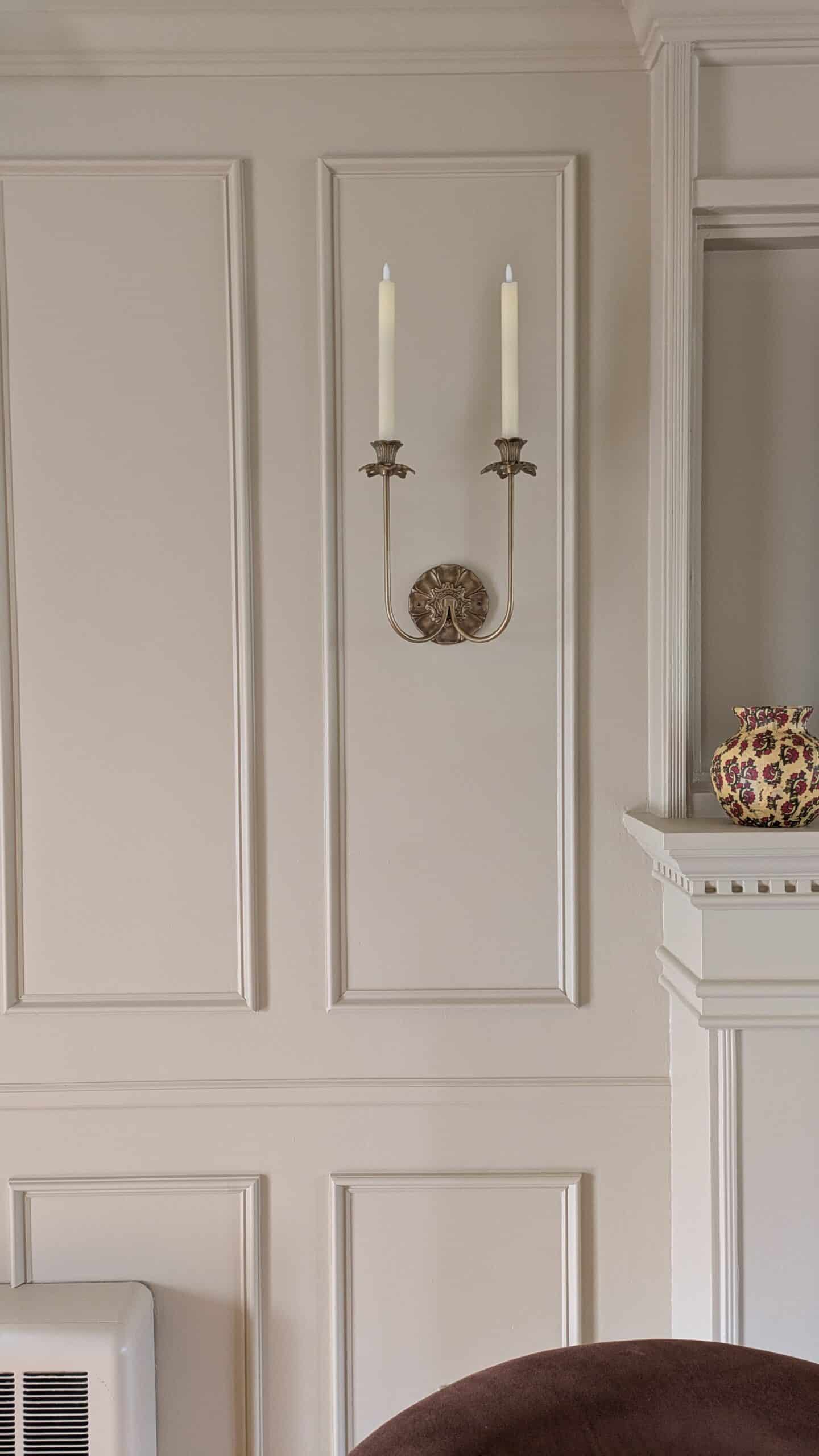 Wall treatment on the living room wall, the paint is a warm honey color drenched. Brass double wall sconce with flameless taper candles on the wal.