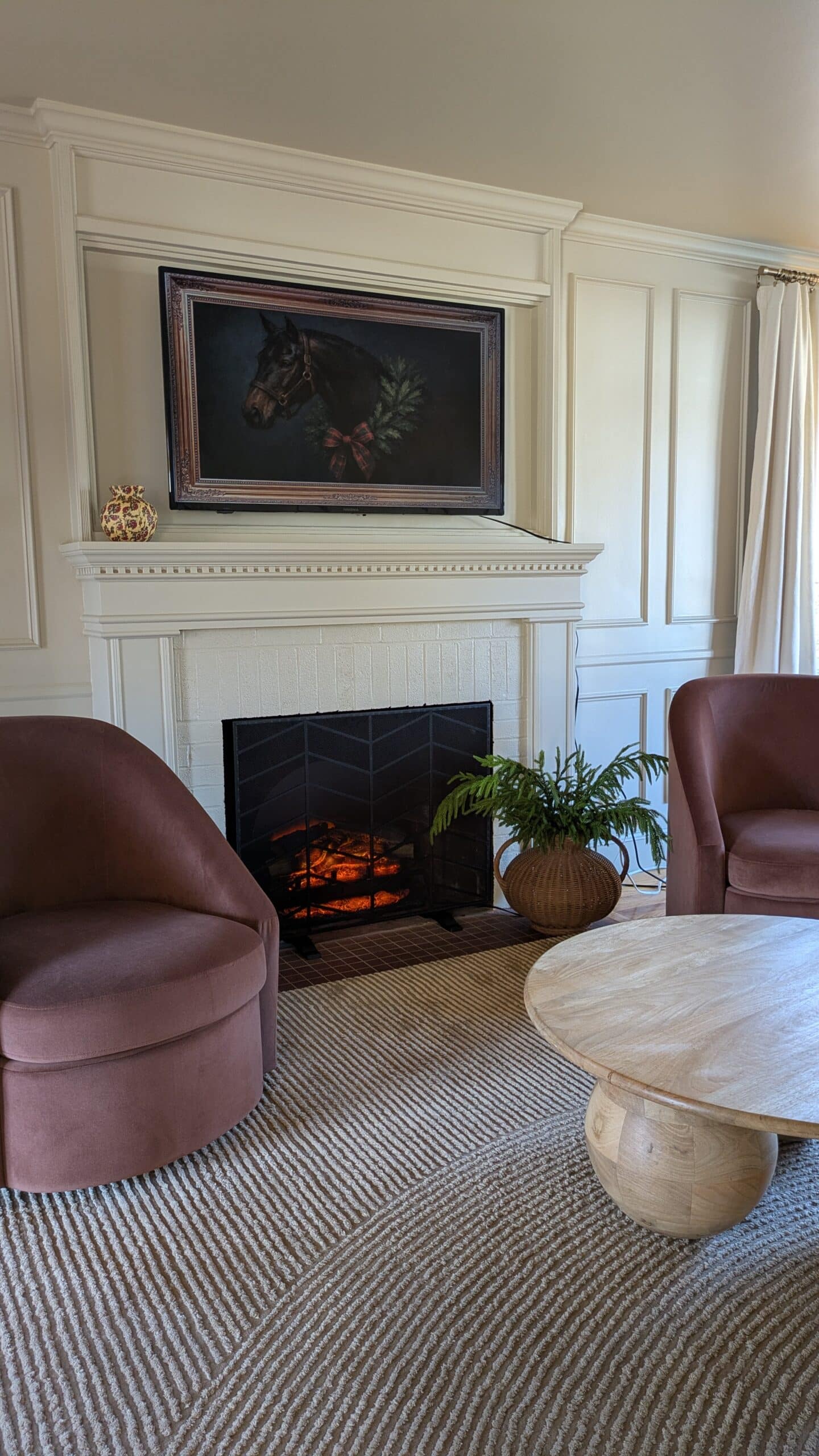 two accent chairs in front of a fireplace with a coffee table. Also tv art above the mantel of a horse.